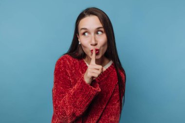 Kırmızı kazaklı kadın mavi arka plana karşı şşşş hareketi yapıyor..