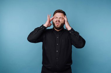 Siyah gömlekli adam mavi arka planda hayal kırıklığı yaşıyor.