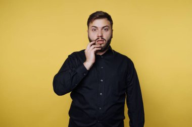 Sarı arka planda siyah gömlekli, şaşırmış bir adam..