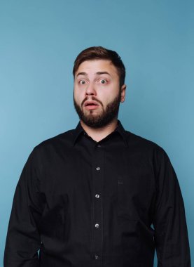 Mavi arka planda siyah gömlekli, sakallı, şaşırmış bir adam..