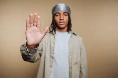 Tarafsız bir arkaplanı olan bir genç stüdyoda duruyor. Kişi ciddi görünürken elini kaldırır. Odaklandıkları nokta jest ve ifadeleri..