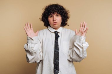 Bir insan ellerini kaldırmış, doğrudan kameraya bakıyor. Resmi bir gömlek ve kravat takıyorlar. Arkaplan sade ve hafiftir ve ışıklandırma onların özelliklerini vurgular..