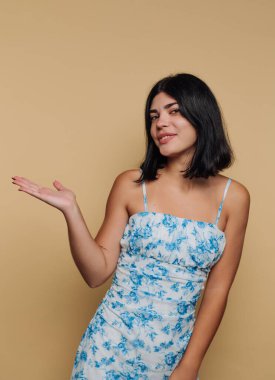 Çiçekli bir elbise giymiş, kendine güvenen bir ifadeyle duran bir kadın. Bir elini misafirperver bir şekilde uzattı ve ortamda dostane bir hava yarattı..