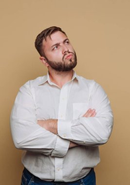 Sakallı bir adam kollarını kavuşturmuş duruyor. Yukarı bakıyor, düşüncelere dalmış. Stüdyonun sade bir arka planı var. Gömleği beyaz ve kot pantolon giyiyor..