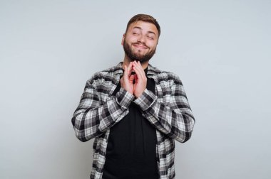 Tarafsız bir geçmişi olan bir adam stüdyo ortamında duruyor. Onun bir sakalı var ve ellerini şakacı bir jest ile birleştirirken gülümsüyor. Gömleği kareli..