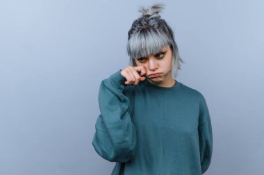 Açık bir arkaplanda gri saçlı ve yeşil kazak giyen bir insan. Gözlerine bakıp hüzünlü bir ifade gösteriyorlar. Sahnede başka kimse ya da nesne yok..