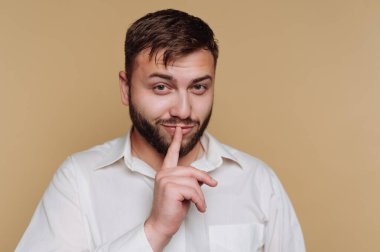 Sakallı bir adam içeride duruyor. Başkalarından sessiz olmalarını istermiş gibi parmağını dudaklarına kaldırdı. Sade bir geçmişi olan tarafsız bir ortamda..