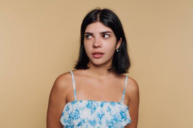 Genç bir kadın koyu renk saçlarıyla özgürce düşüyor. Açık çiçekli bir bluz giyer ve kameradan uzağa bakar. Tarafsız bir arkaplanı vardır..