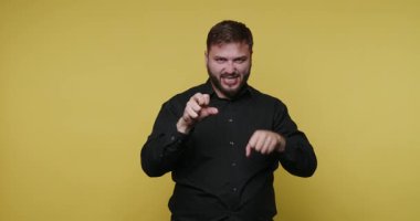 Bir adam fotoğraf stüdyosunda çeşitli el hareketleri yapar. Sarı bir arkaplanın önünde duruyor ve yaratıcı bir ifade takınıyor. Atmosfer canlı ve enerjik..