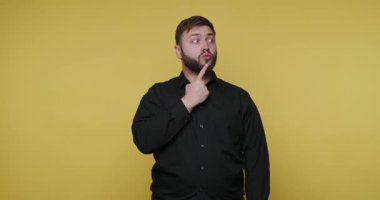 Bir adam sarı bir arka planın önünde, parmakları çenesinde duruyor. Düşünceli görünüyor ve bir şeyler düşünüyor. Gömleği siyah..