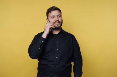 Siyah gömlekli adam telefonda sarı arka planda konuşuyor.