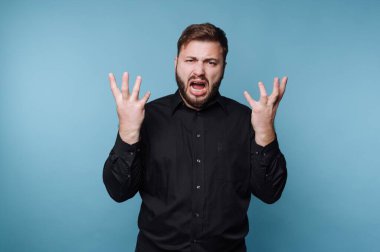 Siyah gömlekli adam mavi arka planda hayal kırıklığı yaşıyor.