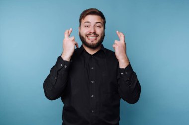 Siyah gömlekli adam mavi arka planda parmaklarını çapraz yapıyor.