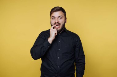 Siyah gömlekli adam sarı arka plana şaşırmış görünüyor.