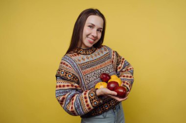 Sarı arka planda elmaları tutan gülümseyen kadın.