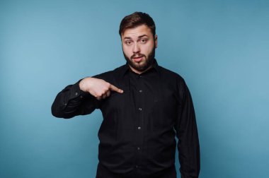 Siyah gömlekli adam mavi arkaplanı işaret ediyor..
