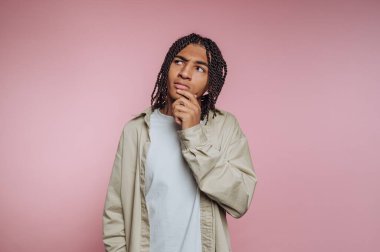 Saçları örgülü, pembe bir arka planı olan genç bir adam..