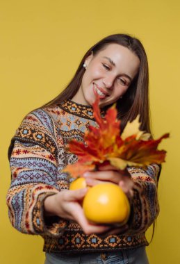 Sarı arka planda gülen kadın, güz yapraklarını ve sarı elmaları tutuyor..