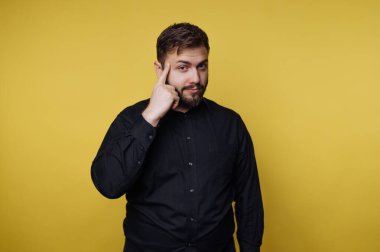 Siyah gömlekli adam sarı arka planda düşünme hareketi yapıyor..
