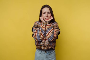 Renkli kazaklı kadın sarı arka planda endişeli görünüyor..