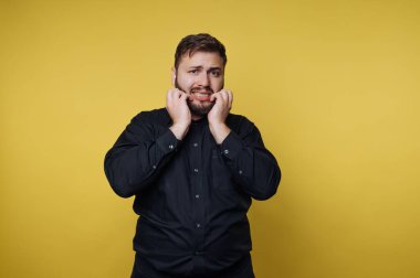 Siyah gömlekli adam sarı arka planda endişeli görünüyor.