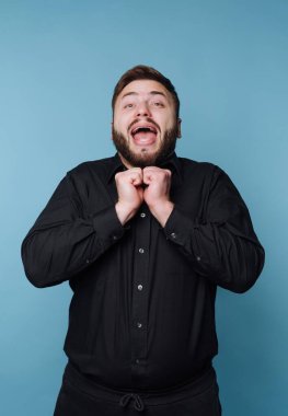Siyah gömlekli adam mavi arka planda heyecan gösteriyor..