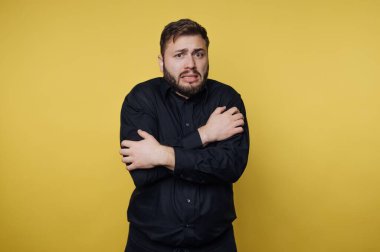 Siyah gömlekli adam sarı arka planda endişeli görünüyor..