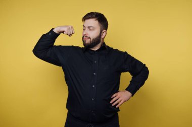 Siyah gömlekli adam sarı arka planda kaslarını esnetiyor..