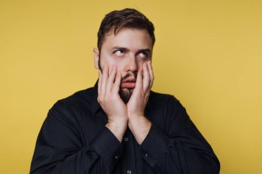 Siyah gömlekli adam sarı arka planda hayal kırıklığına uğramış görünüyor.