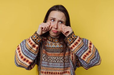 Renkli kazaklı genç bir kadın, sarı bir arka plana karşı üzgün bir yüz ifadesi takınıyor..