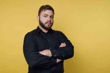 Sarı arka planda kolları çapraz siyah gömlekli kendine güvenen bir adam..