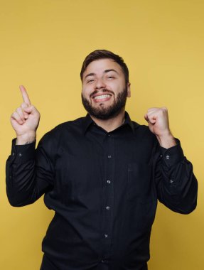 Siyah gömlekli gülümseyen adam sarı arkaplanı işaret ediyor..