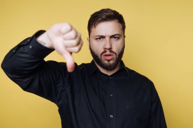 Siyah gömlekli adam sarı arka plana karşı baş parmak işareti yapıyor..