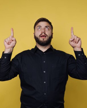 Siyah gömlekli adam sarı arkaplanı işaret ediyor..