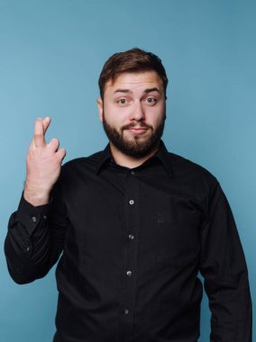 Siyah gömlekli adam mavi arka planda parmaklarını çapraz yapıyor..