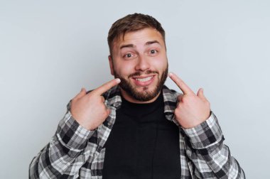 Ekose gömlekli gülümseyen adam gri arka planda yanaklarını gösteriyor..