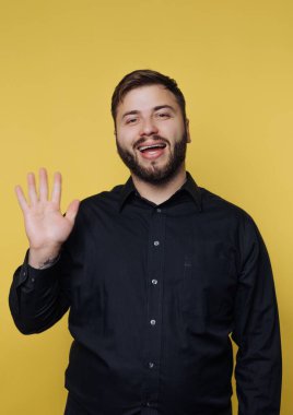 Gülümseyen adam sarı arka plana el sallıyor.
