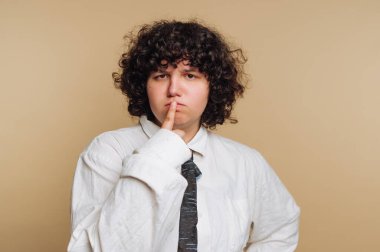 Bej arka planda kıvırcık saçlı, düşünceli bir duruş takınan biri..