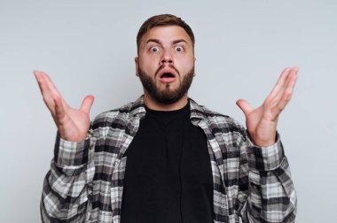 Ağzını açıp ellerini kaldırmış, ekose gömlek giymiş, şaşırmış bir adam..