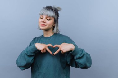 Gri saçlı genç bir kadın elleriyle kalp şekli yapıyor..