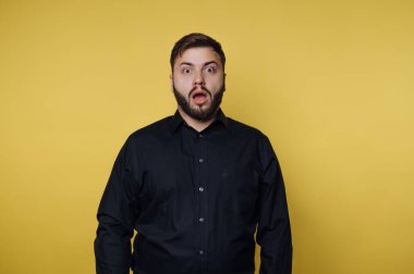 Sarı arka planda siyah gömlekli, şaşırmış bir adam..