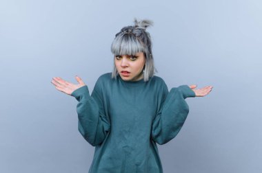 Gri arkaplan üzerinde kafa karışıklığı içinde omuz silken gri saçlı genç bir kadın..