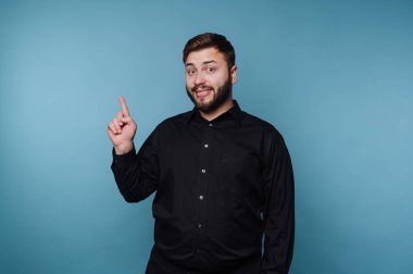Siyah gömlekli gülümseyen adam mavi arkaplanı işaret ediyor..