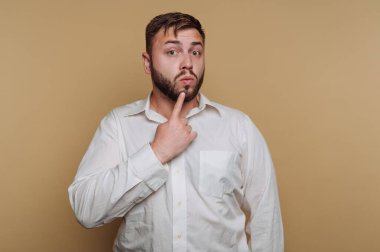 Beyaz gömlekli adam bej arka plana karşı düşünceli bir ifade takınıyor..