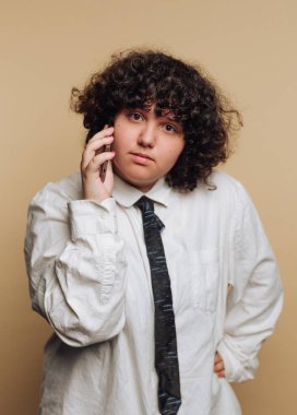 Beyaz gömlekli ve kravatlı, telefonda kıvırcık saçlı biri.