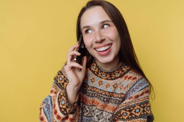 Sarı arka planda telefonla konuşan desenli süveterli, gülümseyen kadın..