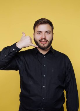 Siyah gömlekli adam sarı arka planda bir telefon hareketi yapıyor..