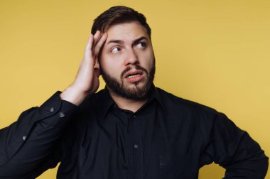 Siyah gömlekli adam sarı arka planda şaşkın görünüyor..