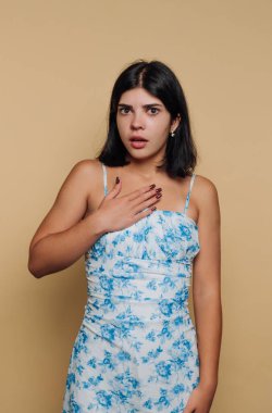 Çiçekli elbiseli kadın bej arka plana şaşırmış görünüyor..