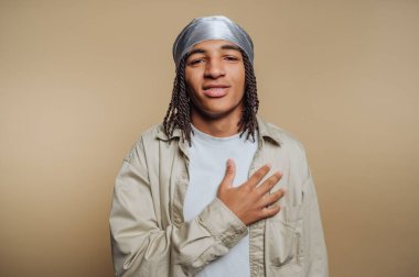 Saçları örgülü, uzun ve günlük kıyafetler giyen genç bir adam..